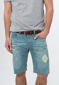 Lyseblå denimshorts med avslappet passform, med frynset stoff og en hem som går rett over knærne. Kombinert med en grå t-skjorte og flettet belte.