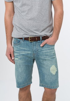 Ljusblå denimshorts med en avslappnad passform, med fransade lappar och en fåll strax ovanför knäet. Tillsammans med en grå t-shirt och flätat bälte.