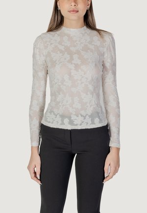 Maglietta bianca a maniche lunghe con sovrapposizione di pizzo floreale, con una silhouette aderente e scollo alto, abbinata a pantaloni neri sartoriali.