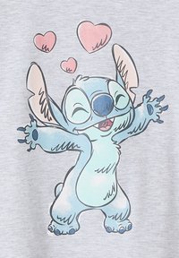 Hellgrau T-Shirt mit einem animierten blauen Charakter mit großen Ohren, der lächelt und die Arme ausstreckt, umgeben von rosa Herzformen.