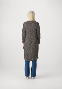 Túnica longa com tecido texturado e multicolorido, com um decote redondo e mangas longas, combinada com jeans azuis flare e saltos altos.