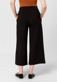 Czarne spodnie szerokie z gładką teksturą, elastycznym pasem i kieszeniami bocznymi. Noszone z płaskimi, błyszczącymi czarnymi butami.