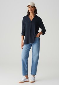 Blusa navy con scollo a V, maniche lunghe e vestibilità comoda, abbinata a jeans dritti azzurri chiari e sneakers bianche.
