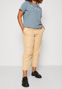 Jasnoniebieska bawełniana koszulka z białym logo, zestawiona z beżowymi spodniami 3/4 i czarnymi sznurowanymi butami. Gładkie tekstury i swobodny design.