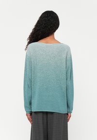 Helles teal Sweatshirt mit strukturiertem Finish, ausgestattet mit langen Ärmeln und einem weit geschnittenen Ausschnitt. Gestaltet mit einem Ombre-Effekt, der von dunkel nach hell übergeht.