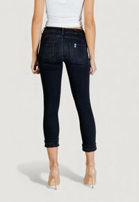 Jeans skinny a lavaggio scuro con risvolti arrotolati e un leggero luccichio, progettati con cinque tasche e una toppa con il logo sulla cintura.