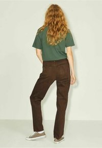 Pantalones de pana marrones con un corte recto, combinados con una camiseta verde. Cuentan con bolsillos traseros y una textura sutil.