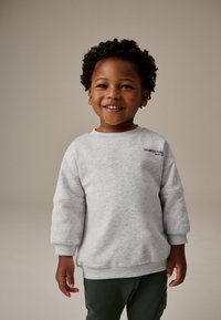 Graues Baumwoll-Sweatshirt mit rundem Ausschnitt und gerippten Bündchen, mit dem schwarzen Stickschriftzug "UNLIMITED FUN" auf der Brust, getragen von einem lächelnden Kind.