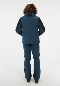 Blauwe geïsoleerde jas met zwarte mouwen en capuchon, met horizontale stiksels en een logo op de schouder. In combinatie met bijpassende broek.