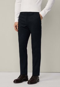 Donkerblauwe visgraatbroek met een slim fit, stoffen textuur, zijzakken en riemlussen, gecombineerd met bruine leren schoenen.