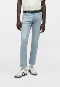 Jeans in denim azzurro chiaro con vestibilità aderente, orli risvoltati e design a cinque tasche, abbinati a una T-shirt bianca e sneakers grigie. Cintura marrone inclusa.