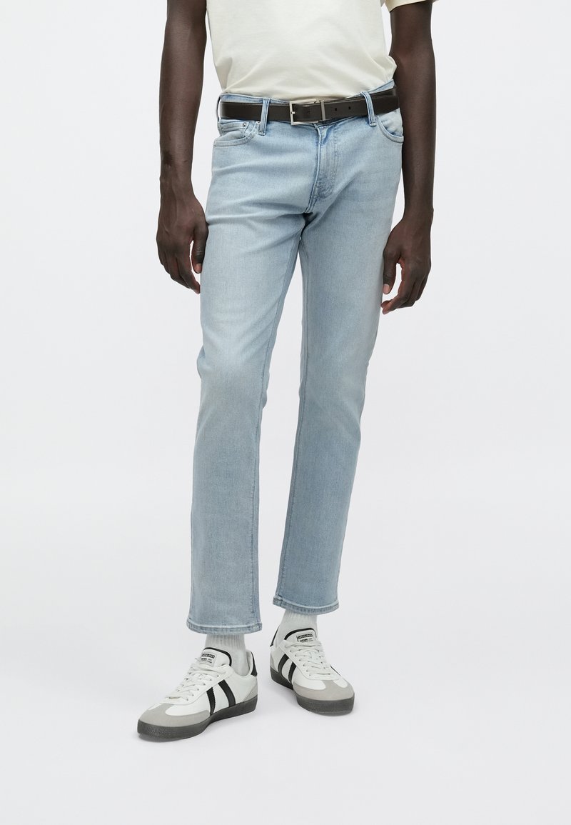 Jeans in denim azzurro chiaro con vestibilità aderente, orli risvoltati e design a cinque tasche, abbinati a una T-shirt bianca e sneakers grigie. Cintura marrone inclusa.