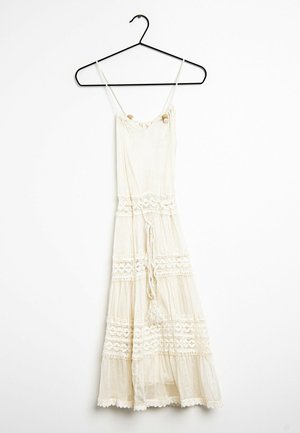 Kremowa sukienka bez rękawów z koronkowymi detalami i plecionym paskiem w talii, wisząca na czarnym drucianym wieszaku na białym tle.