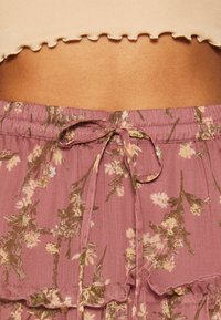 Taille d'une personne portant un crop top beige à volants et une jupe mauve à fleurs avec un ourlet à volants.