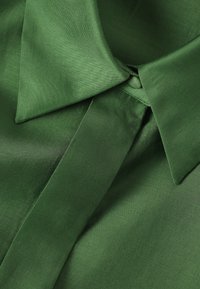 Roheline satiinspikri krae ja lipsu lähivaade, mille sile ja läikiv tekstuur toob esile kangakvaliteedi detailid.