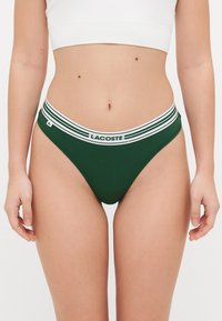 Žalios spalvos medvilninės kelnaitės su baltu juostuotu elastingu dirželiu, kuriame yra "LACOSTE" logotipas. Lygi tekstūra ir prigludęs dizainas.