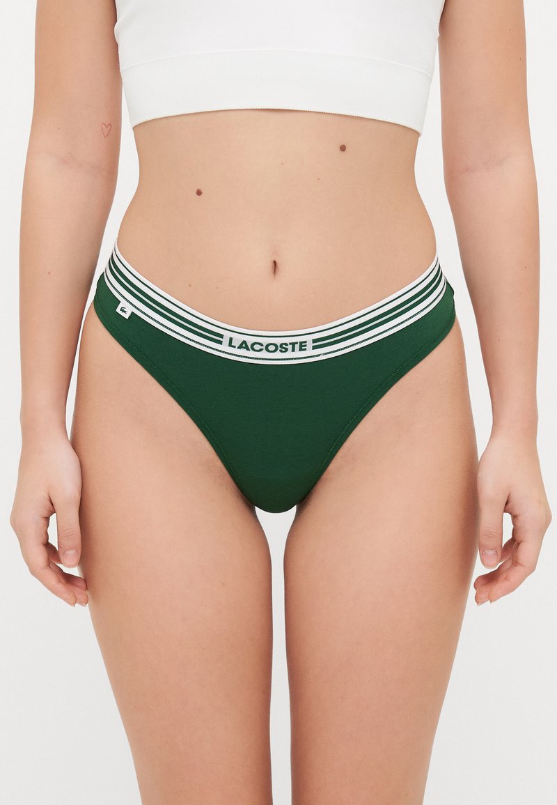 Žalios spalvos medvilninės kelnaitės su baltu juostuotu elastingu dirželiu, kuriame yra "LACOSTE" logotipas. Lygi tekstūra ir prigludęs dizainas.