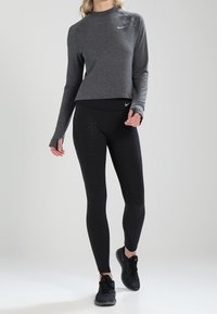 Grijs sportshirt met lange mouwen en een ronde halslijn, voorzien van het Nike-logo, gecombineerd met zwarte, strakke leggings met een gestructureerd ruitpatroon.