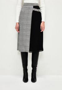 Knee-length skirt with gray plaid and black pleats, belted at the waist with silver buckle, worn with black knee-high boots and white ribbed sweater.