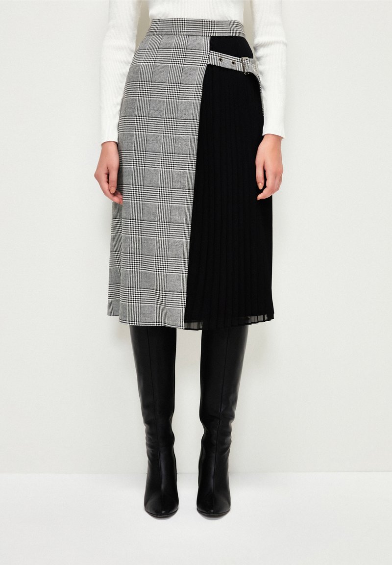 Knee-length skirt with gray plaid and black pleats, belted at the waist with silver buckle, worn with black knee-high boots and white ribbed sweater.