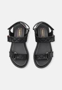 Sandales noires avec dessus synthétique matelassé, deux brides réglables et garniture dorée. Semelles plates avec semelles intérieures noires texturées.