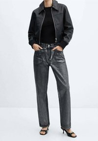 Persona con chaqueta de cuero negra corta, top negro, vaqueros negros desteñidos de talle alto y pierna recta, y sandalias negras de tacón con punta abierta.