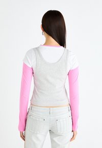 Top ajustado gris sobre una camiseta de manga larga blanca con mangas rosas, combinado con jeans gris claro que tienen bolsillos traseros y detalles laterales.