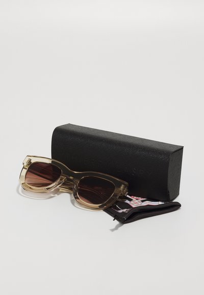 Cat-eye sunglasses in translucent brown frames with dark lenses. Accompanied by a black textured case and a soft pouch for protection.