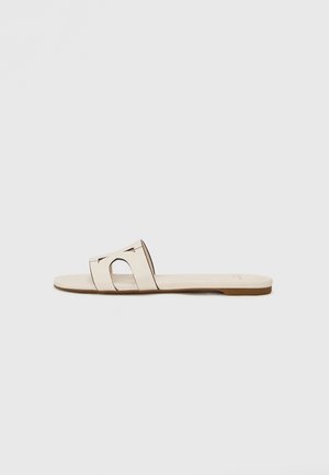 Beige glidesandal med en bred, utskåret stroppdesign med en glatt overflate og flat såle. Minimalistisk stil uten dekorasjoner.
