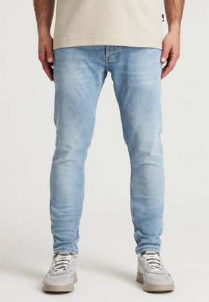 Jeans in denim azzurro chiaro con una vestibilità slim, caratterizzati da una texture sbiadita, cinque tasche e un cinturino standard. Indossati con sneakers grigie.