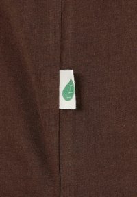 Tissu tricoté marron avec une petite étiquette blanche comportant une icône de feuille verte cousue dans une couture verticale.