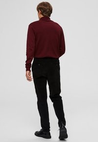 Bordeauxroter Rollkragenpullover, figurbetont, mit langen Ärmeln; kombiniert mit schwarzen Cordhosen und schwarzen Schnürschuhen. Minimalistisches Design.