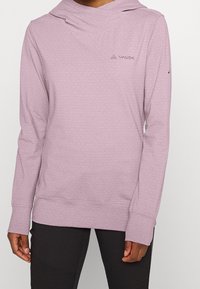 Světle fialová mikina s kapucí vyrobená z měkké látky, s volným límcem, dlouhými rukávy a malými bílými puntíky. Logo VAUDE na levé horní straně.