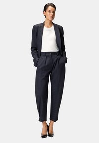 Traje azul marino con rayas finas que incluye una blazer entallada y pantalones de cintura alta. Lleva una blusa blanca ajustada debajo. Tacones negros brillantes completan el conjunto.