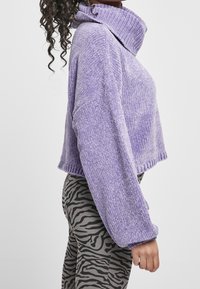 Lila, kurz geschnittenes Sweatshirt mit geripptem Muster und weitem Kragen, kombiniert mit grauen Leggings, die ein schwarzes Zebra-Streifen-Muster aufweisen.