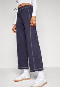 Marineblauwe wijde broek met witte stiksels, elastische tailleband met trekkoord en zijzakken. Gecombineerd met witte sneakers en sokken.