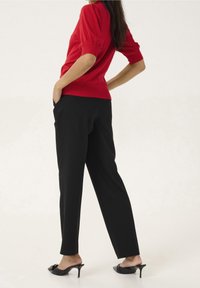 Czerwony sweter z bufkami, w połączeniu z czarnymi spodniami i sandałami na obcasie. Gładka tekstura; dopasowany krój i długość do kostek.