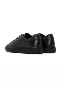 Zapatillas de cuero negro con una superficie lisa, puntera redonda, cordones planos y suela de goma negra texturizada. Diseño simple, forma general de perfil bajo.
