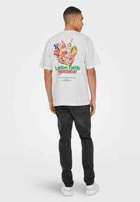 Witte katoenen t-shirt met een kleurrijke illustratie van een winkelwagentje gevuld met boodschappen, met daaronder de tekst "London Fields Superstore".
