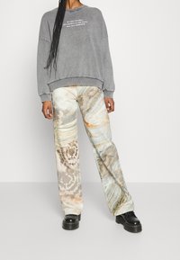 Szara bluza z napisem, zestawiona z szerokimi spodniami o marmurkowym wzorze w pastelowych kolorach. Całość uzupełniają czarne buty na platformie.