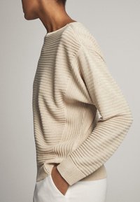 Maglione a coste beige con scollatura rotonda, maniche lunghe e dettagli testurizzati lungo i lati. Tessuto morbido con una vestibilità ampia.