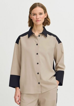 Beige Langarmhemd mit schwarzen Akzenten an Schultern und Ärmeln, mit Knopfleiste und einem oversized, lockeren Schnitt. Glatte Textur.