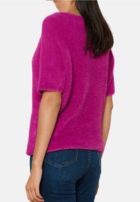 Fuchsiatröja med korta ärmar, mjuk textur och lös passform. Matchad med mörkblå jeans, som visar en rundad nederkant bak.