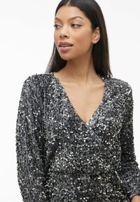 Abito a scollo a V rivestito di paillettes argentate con maniche lunghe, caratterizzato da una morbida texture del tessuto e una silhouette aderente.