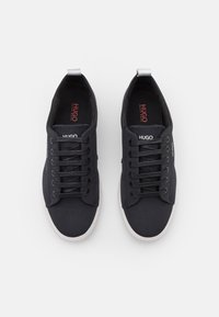 Baskets en toile noire avec semelles en caoutchouc blanches, comportant quatre paires d'œillets, des lacets plats, et un logo sur la languette et le côté.