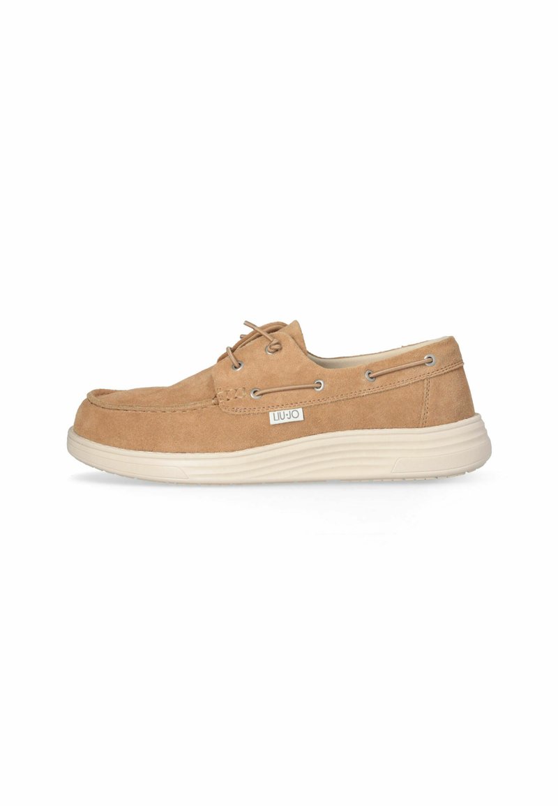Beige Wildlederschuh mit strukturierter Oberfläche, ausgestattet mit silbernen Beschlägen und einer cremefarbenen Gummisohle. Die Schnürsenkel und das Logo sind vorhanden.