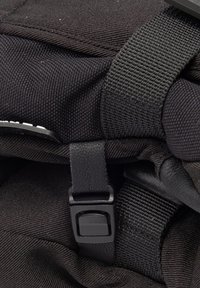 Zaino in tessuto nero con superficie testurizzata, dotato di una fibbia in plastica e spallacci intrecciati per una chiusura sicura e una facile impugnatura.