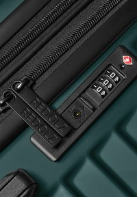 Maleta rígida verde con cremalleras negras, tiradores de cremallera de doble marca y un candado de combinación TSA configurado en 0-0-0.