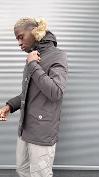 Dark gray hooded jacket with fur trim, button and zip closures, side pockets, and textured fabric, worn over light-colored pants.