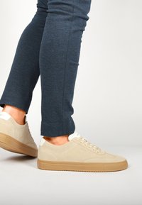 Beige nahkasaappaat, joissa on kerma väri kantapäällä ja vaaleanruskea kumipohja. Kengissä on nauhat ja sileä pinta, yhdistettynä tummansinisiin housuihin.